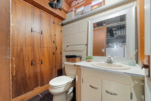 half bathroom featuring vanity, toilet, and concrete block wall