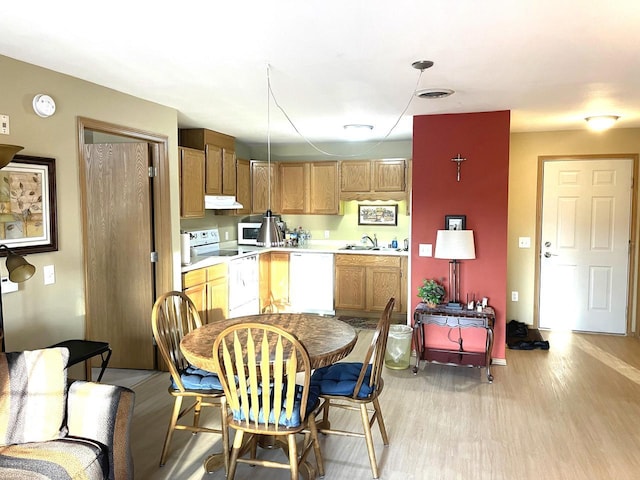 kitchen with under cabinet range hood, light countertops, light wood-style floors, white appliances, and a sink