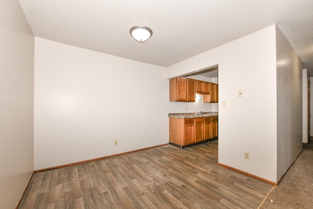 kitchen with brown cabinets, a sink, wood finished floors, light countertops, and baseboards