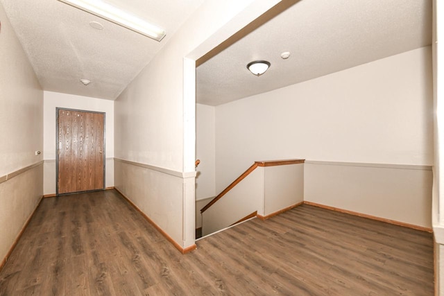 hallway with an upstairs landing, a textured ceiling, and wood finished floors