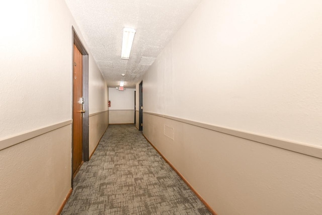 hallway with a textured ceiling, wainscoting, and carpet flooring