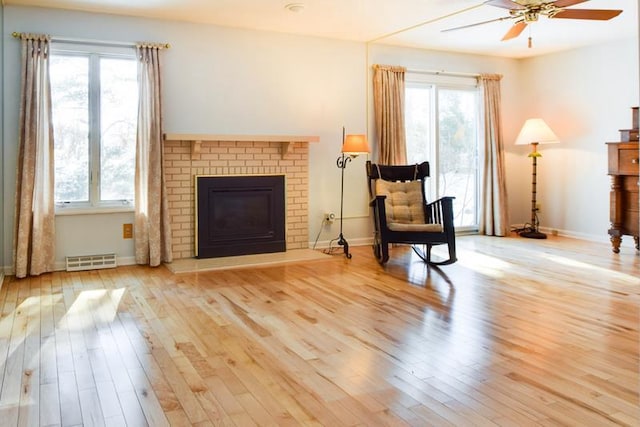 living area with visible vents, wood finished floors, baseboards, a brick fireplace, and ceiling fan