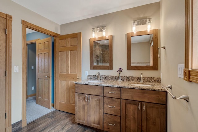 full bath featuring double vanity, tiled shower, wood finished floors, and a sink