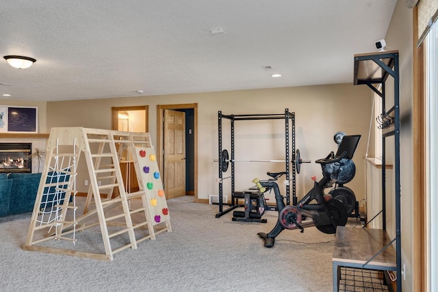 workout area featuring baseboards, carpet, recessed lighting, a glass covered fireplace, and a textured ceiling