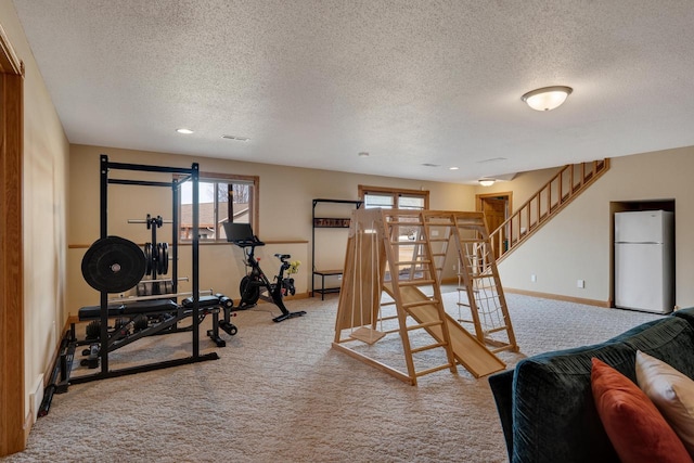 workout room featuring light colored carpet, a textured ceiling, and baseboards