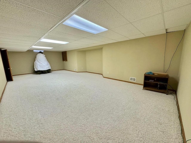 finished below grade area featuring visible vents, carpet, baseboards, and a drop ceiling