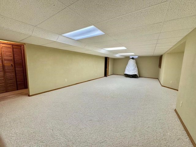 finished below grade area featuring a drop ceiling, baseboards, and carpet