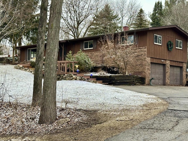 view of front facade with brick siding, driveway, a chimney, and a garage