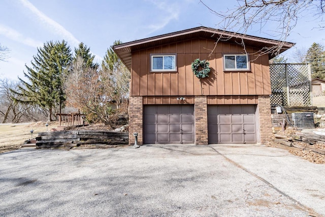 view of property exterior with brick siding, driveway, a garage, and board and batten siding