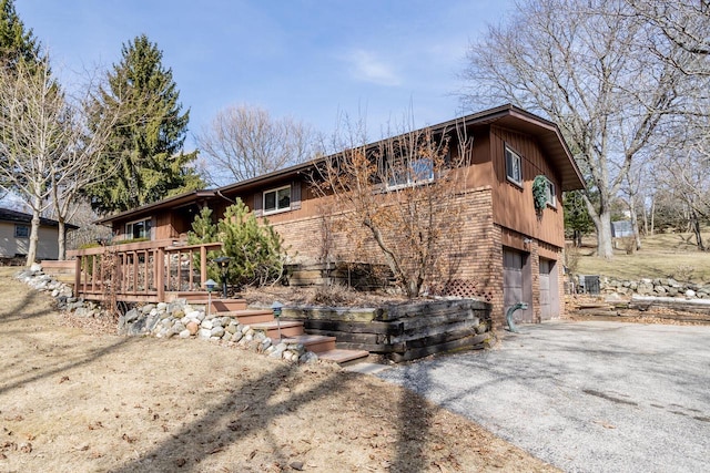 exterior space featuring brick siding, an attached garage, aphalt driveway, and a deck