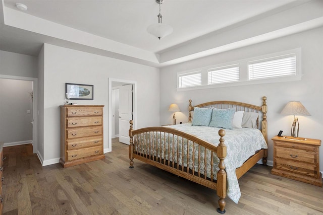 bedroom with a tray ceiling, wood finished floors, and baseboards