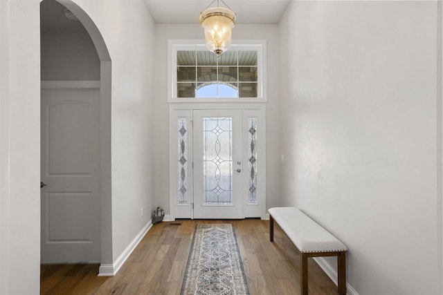 foyer entrance with baseboards, arched walkways, and wood finished floors