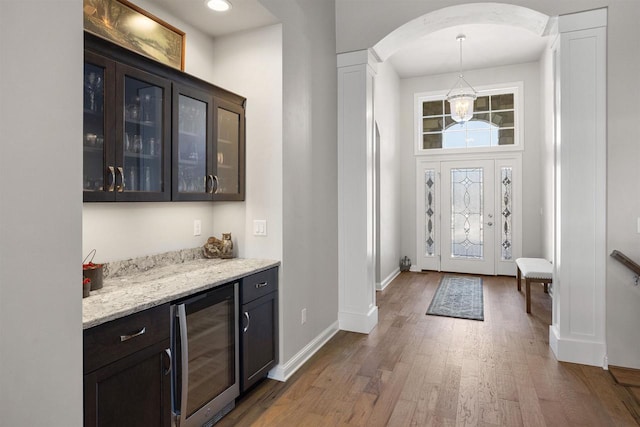 entryway featuring wood finished floors, baseboards, arched walkways, wine cooler, and a dry bar