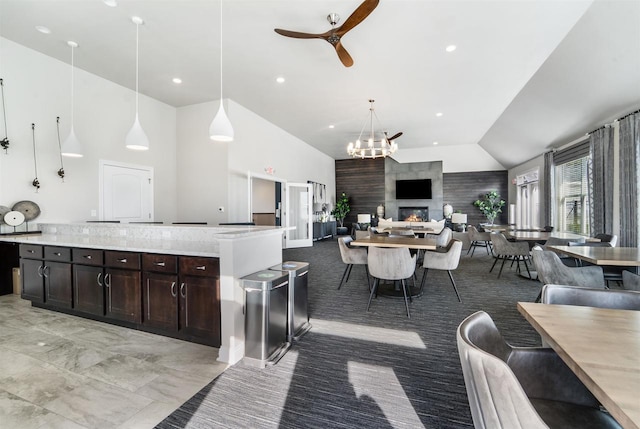 kitchen featuring high vaulted ceiling, ceiling fan with notable chandelier, open floor plan, dark brown cabinets, and hanging light fixtures