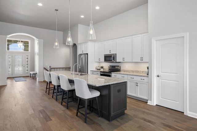 kitchen featuring arched walkways, stainless steel appliances, a high ceiling, and an island with sink