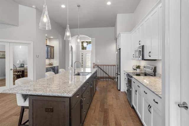 kitchen with a spacious island, arched walkways, a sink, white cabinets, and appliances with stainless steel finishes