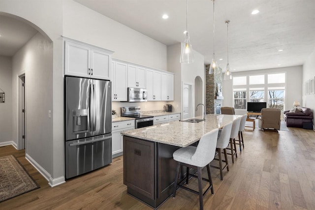 kitchen with a sink, appliances with stainless steel finishes, arched walkways, white cabinetry, and dark wood-style flooring