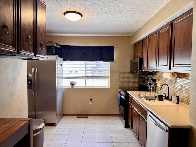 kitchen featuring a sink, a textured ceiling, appliances with stainless steel finishes, light tile patterned floors, and decorative backsplash