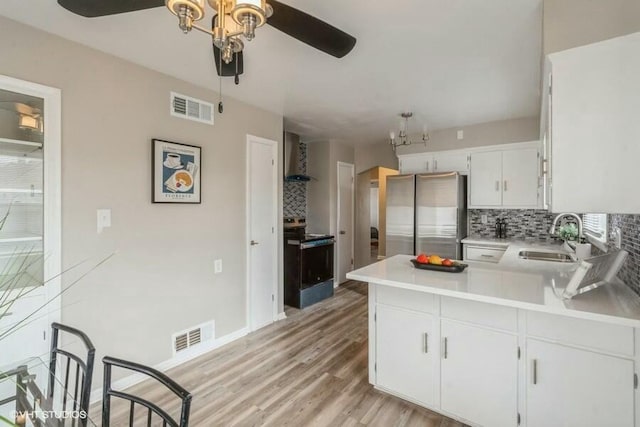 kitchen with visible vents, a sink, decorative backsplash, stainless steel appliances, and wall chimney range hood