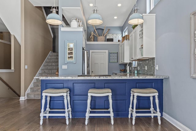 kitchen with baseboards, dark wood-style flooring, white cabinets, a kitchen breakfast bar, and tasteful backsplash