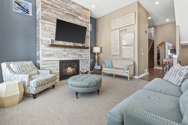 living room featuring baseboards, stairs, a stone fireplace, recessed lighting, and arched walkways