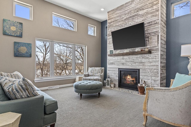 carpeted living area with a stone fireplace, visible vents, baseboards, and a towering ceiling