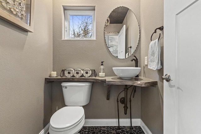 half bath with a sink, baseboards, toilet, and a textured wall