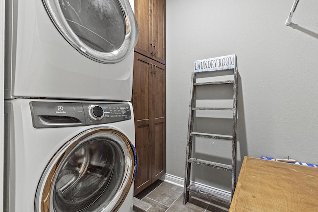 washroom with cabinet space, baseboards, and stacked washer and dryer