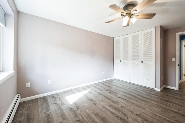 unfurnished bedroom with a baseboard heating unit, baseboards, a closet, and wood finished floors