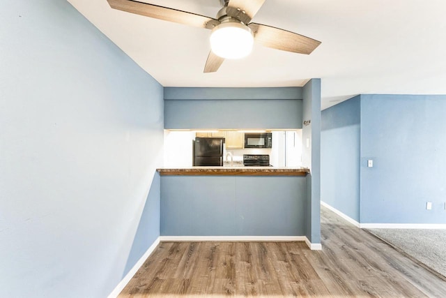 interior space with black appliances, a ceiling fan, baseboards, and wood finished floors