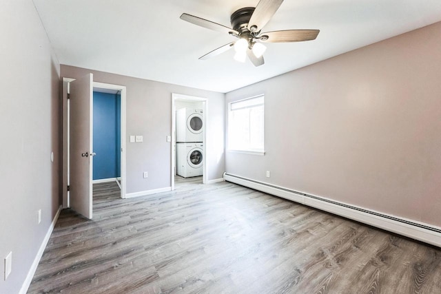 unfurnished bedroom featuring stacked washer and dryer, wood finished floors, baseboards, and a baseboard radiator