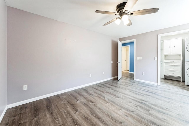 unfurnished bedroom with ceiling fan, baseboards, wood finished floors, a closet, and stacked washer / drying machine