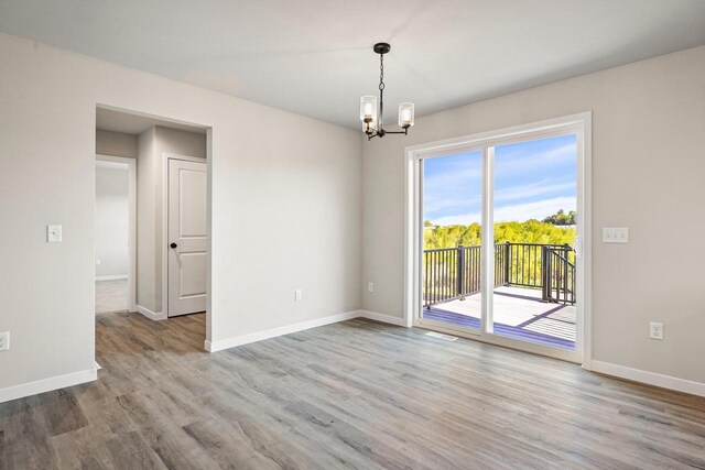 spare room featuring an inviting chandelier, baseboards, and wood finished floors