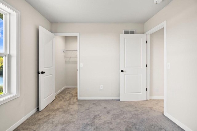 unfurnished bedroom with a spacious closet, baseboards, visible vents, and carpet floors