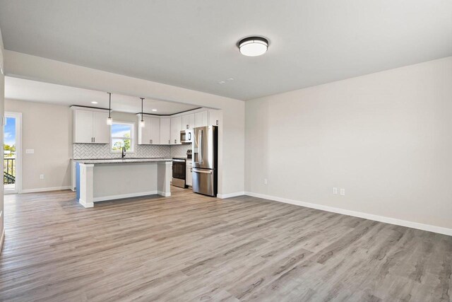 kitchen featuring open floor plan, backsplash, stainless steel appliances, and light wood-style floors