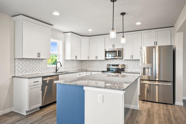 kitchen featuring a sink, wood finished floors, a center island, stainless steel appliances, and white cabinets