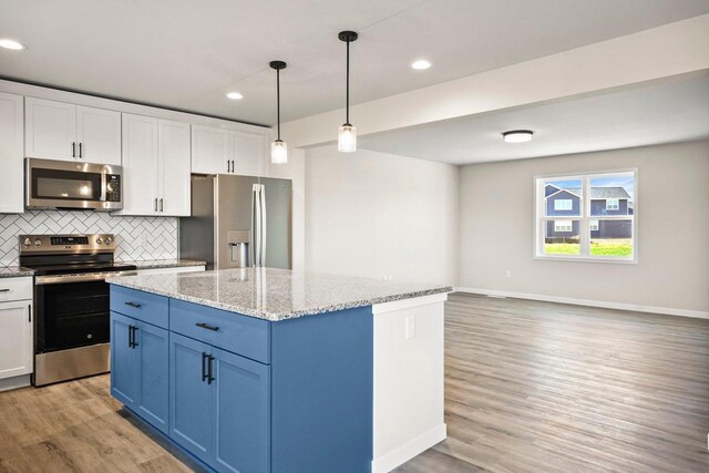 kitchen with light wood finished floors, decorative backsplash, white cabinets, appliances with stainless steel finishes, and a center island