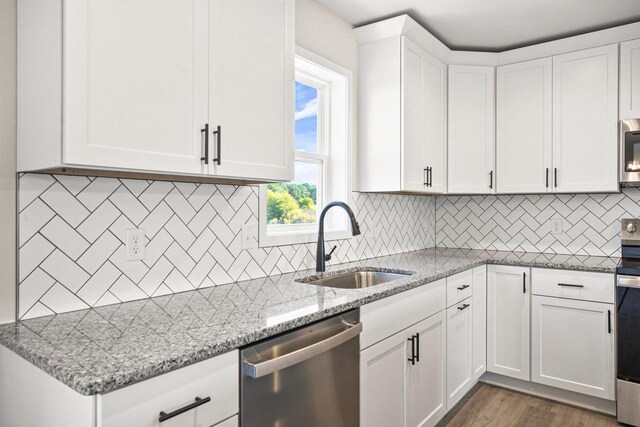 kitchen with a sink, light stone counters, appliances with stainless steel finishes, white cabinets, and dark wood-style flooring