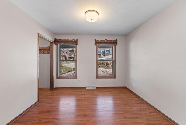 unfurnished room with baseboards, visible vents, and wood finished floors