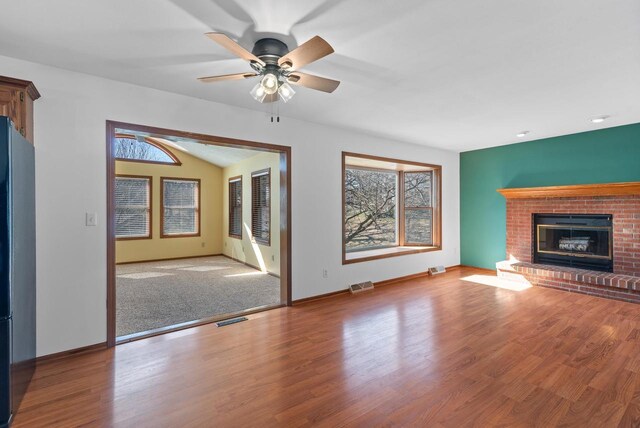 unfurnished living room featuring a brick fireplace, visible vents, a ceiling fan, and wood finished floors