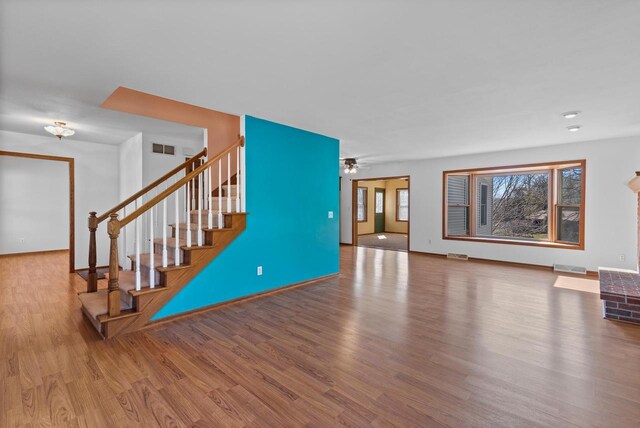 living area with a ceiling fan, visible vents, stairs, and wood finished floors