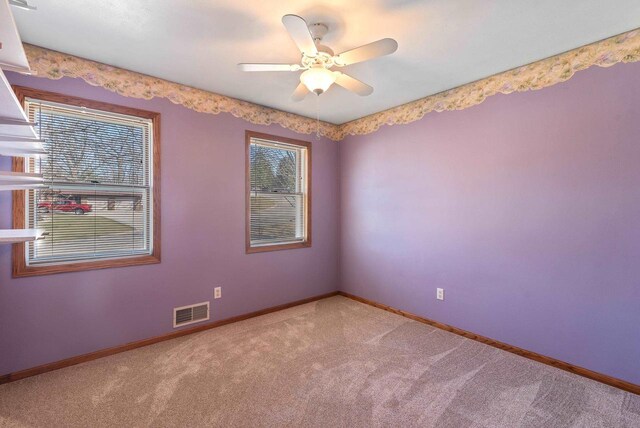 spare room featuring carpet floors, baseboards, ceiling fan, and visible vents