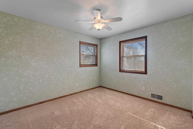 carpeted spare room featuring baseboards, visible vents, a ceiling fan, and wallpapered walls