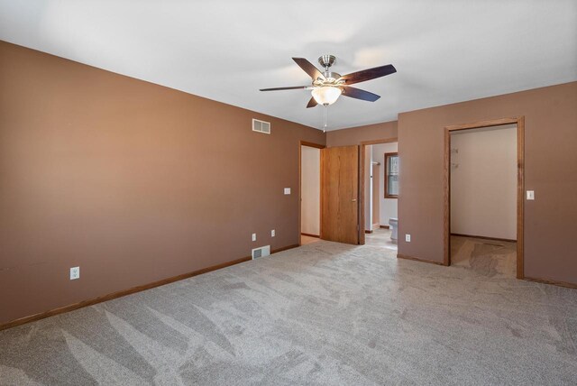 unfurnished bedroom featuring a walk in closet, carpet, baseboards, and visible vents