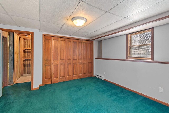 unfurnished bedroom with carpet floors, baseboards, a baseboard heating unit, and a drop ceiling