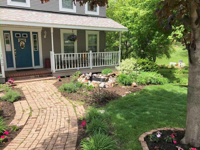 view of exterior entry featuring a lawn, covered porch, and roof with shingles