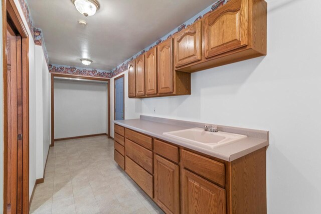 kitchen featuring light countertops, a sink, baseboards, and brown cabinetry