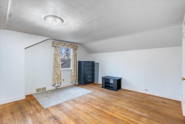 bonus room with baseboards, visible vents, lofted ceiling, light wood-style floors, and a textured ceiling