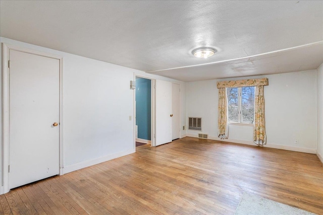 unfurnished bedroom featuring visible vents, heating unit, a textured ceiling, light wood-style floors, and baseboards