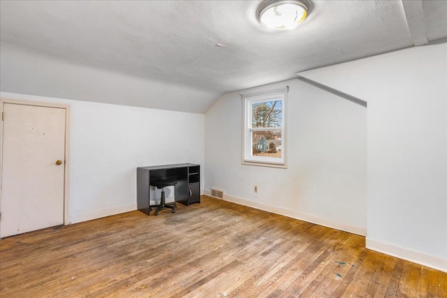 additional living space with visible vents, a textured ceiling, wood-type flooring, baseboards, and vaulted ceiling